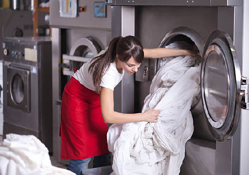 Female worker in laundry service,get washed sheets out of washing machine