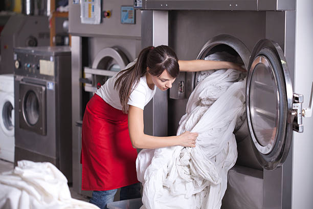 Female worker in laundry service,get washed sheets out of washing machine